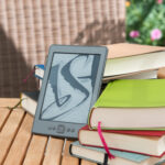 An e-reader propped against a pile of books.
